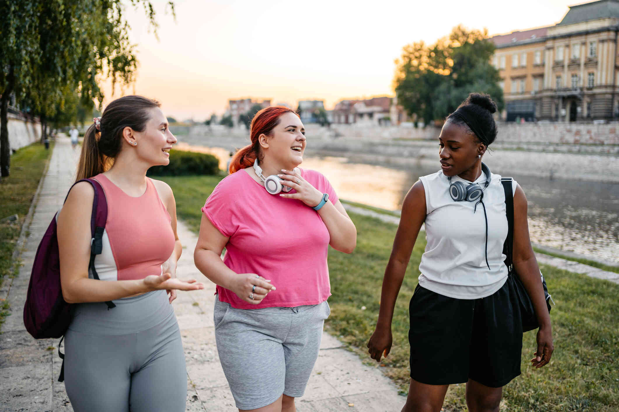 Three women in workout attire smile as they walk next to each other down an outdoor, waterfront path.